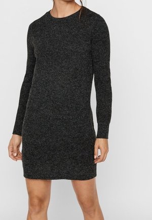 Femme portant une robe-pull en maille gris foncé, à manches longues et longueur genoux, avec un col rond, debout devant un fond uni.
