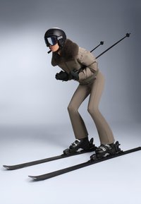 Completo da sci composto da una giacca imbottita marrone chiaro con colletto in pelliccia, pantaloni marroni aderenti, scarponi da sci neri e bastoncini da sci neri, su sfondo neutro.