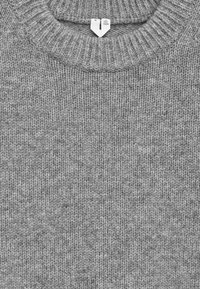 Grauer gestrickter Pullover mit einem gerippten Halsausschnitt und Struktur in mittlerem Gewicht. Pflegeetikett sichtbar am Kragen.