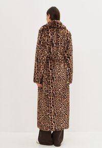 Abrigo de pelaje falso con estampado de leopardo, corte ceñido en la cintura, mangas largas y cuello con muescas, que presenta una textura suave en tonos marrones y negros.