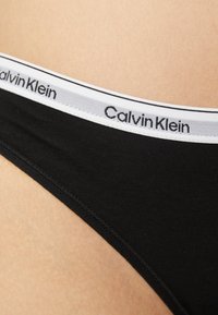 Zwarte katoenen bikinislip met een witte elastische tailleband waarop het logo "Calvin Klein" staat. Gladde textuur, low-rise ontwerp.