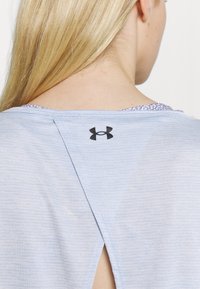 Vaaleansininen urheilu paita, joka on valmistettu hengittävästä kankaasta. Takana on halkio ja yläselässä on musta logo. Pintakuvioitu viimeistely.