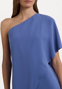 Asymmetrisk klänning i mjukt blått tyg, med en axel, slät yta och draperad design med en något snedställd fåll.