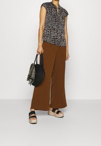 Blusa de manga corta con estampado de animales en negro y marrón, pantalones de pierna ancha marrones, sandalias de plataforma negras y un bolso redondo de tejido negro con una bufanda.