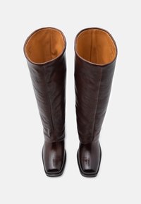 Καφέ δερμάτινες μπότες μέχρι το γόνατο με τετράγωνη μύτη, λεία υφή και πορτοκαλί επένδυση, με μινιμαλιστικό σχέδιο και χωρίς ορατά εξαρτήματα.