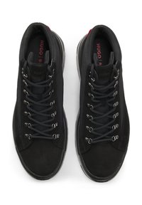 Zapatillas negras de caña alta con parte superior de ante y tela, cordones multitonales, ojales de metal y un logo rojo contrastante en la plantilla.