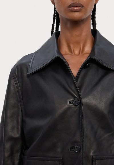 Must mustrind nahkjakker suurte krae, kahe nupuga ja küljetaskutega. Sile tekstuur ja kohandatud disain, millel on detailid kaela piirkonnas.