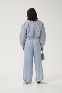 Giacca bomber grigia con orlo a costine, abbinata a jeans a gamba larga blu chiaro. Una piccola borsa blu è tenuta in una mano.