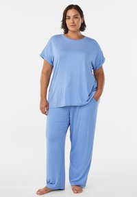 Vaaleansininen rento vaatesetti, johon kuuluu lyhythihainen yläosa käännetyin kalvosin ja väljät housut sivutaskuilla, valmistettu pehmeästä kankaasta.