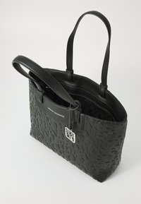 Black tote bag with textured lettering design, leather material, dual handles, and a zippered top. Features embossed logo and inside pockets.