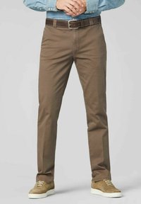 Bruine chino broek met een rechte pijp, gemaakt van katoen, met een riem met een zilveren gesp en gedragen met lichtbruine sneakers.