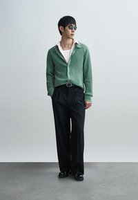 Πράσινη ριγωτή ζακέτα, λευκό πουκάμισο, μαύρο παντελόνι ραμμένο και μαύρα παπούτσια. Χαρακτηρίζεται από κάθετη υφή και χαλαρή εφαρμογή.