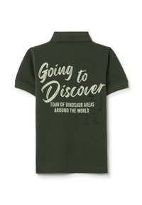 Polo de color verde oscuro con un estampado gráfico que incluye el texto "Voy a Descubrir" y una ilustración de un dinosaurio en la parte posterior.