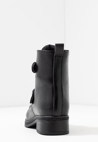 Botín de cuero negro hasta el tobillo con textura suave, con cremallera lateral y punta redondeada. Cuenta con un pequeño tacón y acentos decorativos en el costado.