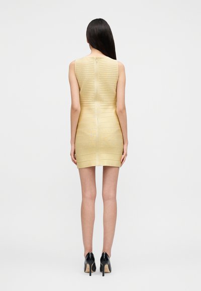 Πλεκτό κίτρινο φόρεμα με οριζόντιες ρίγες, χωρίς μανίκια και φερμουάρ στο πίσω μέρος. Φορεμένο με μαύρα ψηλοτάκουνα παπούτσια.