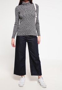 Grau gestrickter Rollkragenpullover mit taillierter Passform, kombiniert mit dunkelblauen, weit geschnittenen Jeanshosen und weißen Sneakers. Minimale Accessoires enthalten.