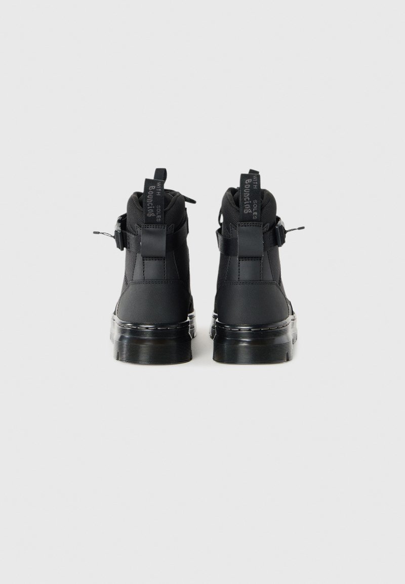 Une paire de bottines noires avec semelles robustes, languettes arrière portant l'inscription "AVEC SEMELLES REBONDIS" et sangles à boucle sur les côtés, le tout sur un fond blanc.