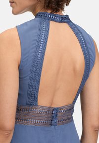 Blaues Kleid mit tiefem Rückenausschnitt, dekorativer Spitzenborte und strukturiertem Stich entlang der Schultern und Taille für zusätzliche Details.