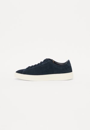 Marineblaue Wildleder-Sneaker in niedriger Ausführung mit schwarzen Schnürsenkeln und einer dicken weißen Gummisohle vor weißem Hintergrund.
