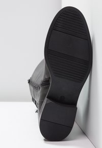 Bota de cuero negro con suela de goma plana, texturizada para mayor agarre, y cierre de cremallera en el lateral. Talla marcada como 37.