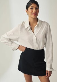 Hvidstribet button-up skjorte med lange ærmer, parret med en sort nederdel. Glat stof, afslappet pasform og synlige knapdetaljer.