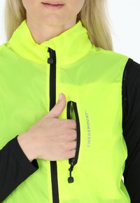 Fluorescencyjna żółta kamizelka z wysokim kołnierzem, czarnym zamkiem i kieszenią na zamek błyskawiczny na klatce piersiowej. Wykonana z lekkiego, gładkiego materiału i z detalem logo.