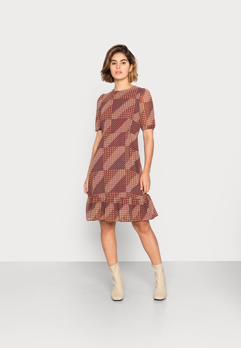 Vestido estampado com mangas curtas em balão, com barra assimétrica, nas tonalidades de vermelho, castanho e creme, apresentando formas geométricas e acentos circulares.