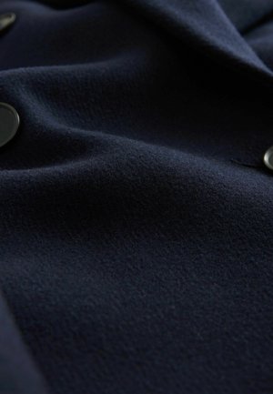 Námornícky vlnený látka s textúrovaným povrchom a jemným leskom. Obsahuje okrúhle čierne gombíky pozdĺž okraja, ktoré sa vyznačujú aerodynamickým dizajnom.