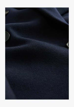 Tumesinine villakangas, millel on tekstureeritud pind ja õrn läige. Servas on ümmargused mustad nupud, mis näitavad voolujoonelist disaini.