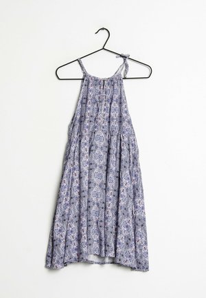 Robe d'été sans manches à motifs bleus et blancs avec bretelles spaghetti suspendue sur un cintre en fil de fer noir contre un fond blanc.