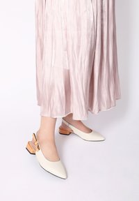 Hvide slingback sko med spids tå, med en tekstureret sål og en orange detalje på den lave blokhæl.