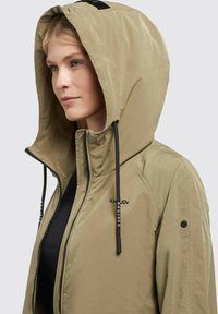 Giacca khaki con cappuccio dal finish testurizzato, dotata di lacci neri, chiusura con zip e logo ricamato sul petto.