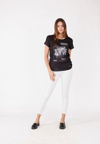 Camiseta negra con un diseño gráfico de palmeras y texto, combinada con vaqueros ajustados blancos y mocasines negros. Estilo minimalista.