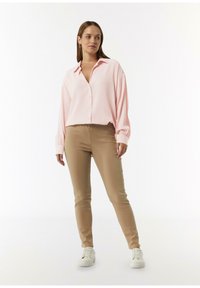 Lichtroze button-up shirt met ribbelstructuur, gecombineerd met tan skinny broek en witte sneakers. Het shirt heeft een kraag en lange mouwen.