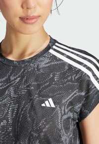 Černé a šedé sportovní tričko s hadím vzorem, kulatým výstřihem, krátkými rukávy a třemi bílými pruhy na ramenou.