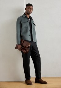 Gray wool blend jacket with front pockets, black shirt, black trousers, brown leather bag, and brown suede ankle boots. Smooth textures.