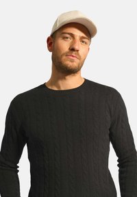 Czarny sweter w splot warkocza z długimi rękawami i okrągłym dekoltem, w zestawie z jasnym, teksturowanym czapką baseballową.