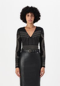 Svart bodysuit med lange ermer som har metalliske naglemønstre, kombinert med et høyt liv sort skinn blyantskjørt med belte.
