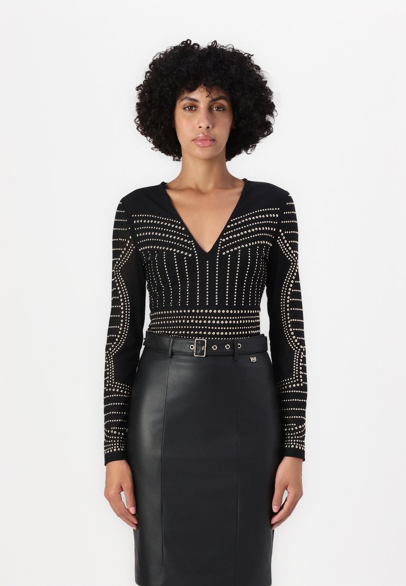 Svart bodysuit med lange ermer som har metalliske naglemønstre, kombinert med et høyt liv sort skinn blyantskjørt med belte.