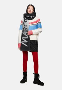 Oversized knitted sweater with red, blue, and black stripes, paired with a black graphic scarf, quilted black skirt, red tights, and black boots.
