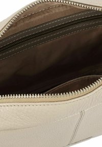 Interior de un bolso de mano de cuero color beige con un acabado texturizado, que cuenta con una cremallera suave y dos bolsillos con cremallera. El forro es de un marrón claro sólido.