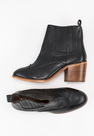 Zwarte leren enkellaarzen met een brogue-ontwerp, geribbelde elastische zijpanelen en een houten blokhak. Gladde textuur en gepolijste afwerking.