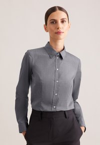 Camicia grigia a maniche lunghe con bottoni, colletto strutturato, leggera texture e bottoni abbinati, abbinata a pantaloni scuri.