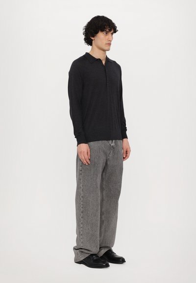 Polo shirt noir à manches longues avec col, associé à un jean en denim gris ample et des chaussures noires. Texture lisse tout au long.