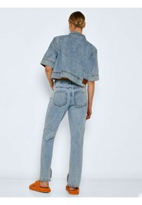 Jaqueta de ganga com mangas curtas e design cropped, combinada com jeans de perna reta. Lavagem clara e textura lisa, com bolsos traseiros.