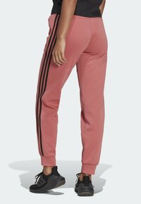 Roze joggers met zwarte zijstripes, gemaakt van zacht materiaal. Heeft een elastische tailleband en taps toelopende benen. Gecoördineerd met zwarte sportschoenen.