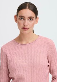 Lys rosa genser med ribbestruktur og subtilt kabelstrikkedesign, med rund hals og trekvart-ermer.