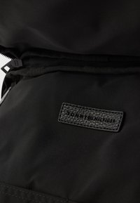 Čierna bunda s textúrovanou čiernou nášivkou s vystaveným nápisom "TOMMY HILFIGER", hladká tkanina a viditeľné detaily zipsu.