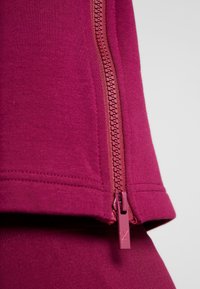 Přiléhavý vínový svetr s hladkou texturou, středovým zipem a odpovídajícím jezdcem na zipu. Jednoduchý design bez dalších vzorů.