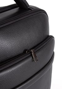 Musta nahkakassi, jossa on teksturoitu pinta, varustettuna kaksinkertaisella vetoketjulla ja pyöreällä muodolla. Koristeluina ovat sileät vetoketjut ja ompelusyksityiskohdat.